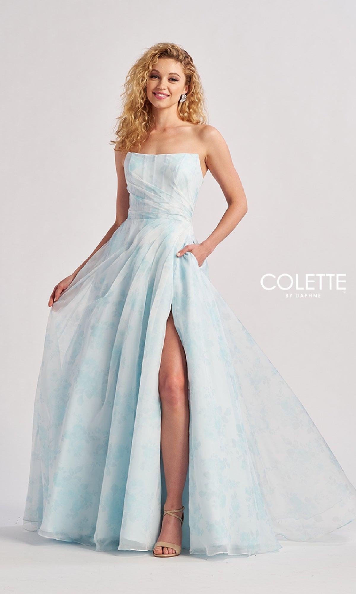 A woman models the Long Prom Dress: Colette CL8635, a strapless light blue floral pastel gown with a thigh-high slit, standing against a plain background with